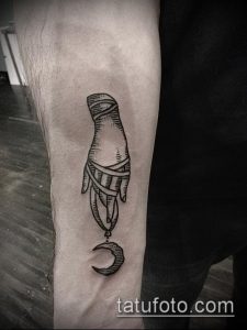 Фото тату в стиле blackwork, изображающее руку, держащую полумесяц. Татуировка выполнена черными чернилами и имеет четкие контуры.