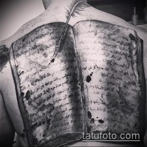 Фото татуировки, изображающей открытую книгу на спине человека. Детализированный рисунок с пером и текстом, выполненный в реалистичном стиле.