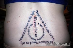 Фото тату на пояснице с цитатой из Гарри Поттера и символом Даров Смерти, выполненное черными чернилами в минималистичном стиле.