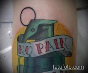 Фото тату гранаты в стиле олдскул с надписью 'No Pain' на желтом фоне. Яркий и красочный рисунок татуировки на руке.