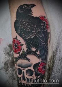Фото татуировки на предплечье с изображением ворона, сидящего на черепе, окруженного красными розами. Татуировка выполнена в стиле олдскул.