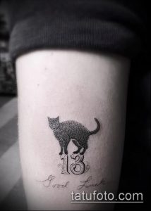Фото тату: черный кот сидит на цифре '13', под которой надпись 'Good Luck'. Черно-белый рисунок татуировки в реалистичном стиле.
