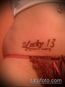 Фото татуировки надписи 'Lucky 13' красным цветом на бедрах.