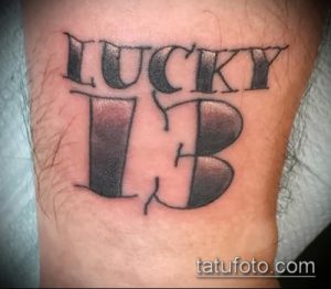 Фото тату надписи 'Lucky 13' в классическом стиле, выполненное на руке в черных тонах.