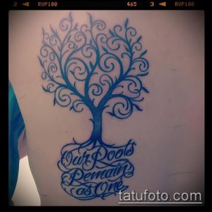 Фото тату: красивое тату дерева в синих тонах с изящной надписью "Our Roots Remain as One" на боку.