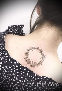Фото тату: детализированный рисунок цветочного венка с лавровыми листьями на женской лопатке. Эскиз татуировки в стиле ботаника с добавлением цветочных элементов.