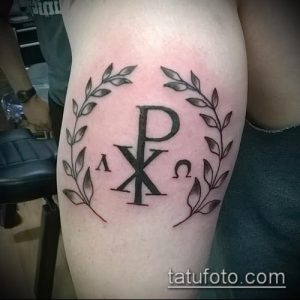 Фото тату: символ Chi Rho (XP) в окружении лаврового венка на руке. Религиозная татуировка в классическом стиле с мягкими линиями.