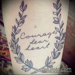 Фото тату: надпись "Courage, dear heart" в обрамлении веночка из листьев на предплечье. Элегантный и вдохновляющий рисунок татуировки.