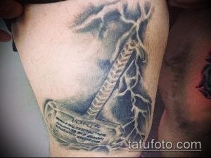 Фото татуировки на бедре с изображением молота Тора, выполненного в технике blackwork. Детализированный рисунок татуировки с использованием только черного цвета.