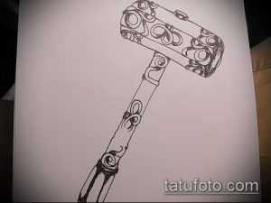 Фото эскиза татуировки: стилизованный молот с завитками и узорами, выполненный черными линиями.