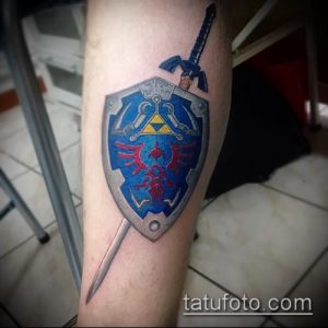 Фото тату на руке: щит и меч из игры The Legend of Zelda, выполненные в ярких цветах. Игровой рисунок татуировки для фанатов.