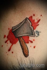 Татуировка топора с красными брызгами, имитирующими кровь. Рисунок выполнен в реалистичном стиле с использованием теней и полутонов.