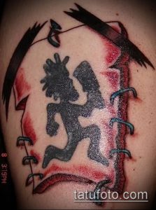 Фото тату с изображением персонажа Violent J из группы Insane Clown Posse на плече, выполненное в черных тонах с красными брызгами.