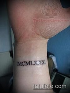 Фото тату римскими цифрами MCM LXX XI на запястье. Черный контур, тонкие линии, минималистичный дизайн, небольшое расположение.