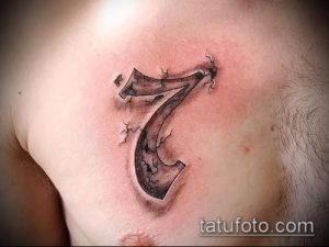 Фото тату: черная татуировка цифры 7 на груди мужчины. Цифра выполнена в стильном и лаконичном дизайне, с эффектом трещин.