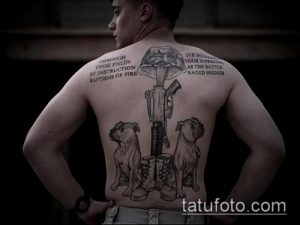 Фото тату на спине с изображением военного шлема, двух собак и оружия. Черно-серый рисунок с надписями.