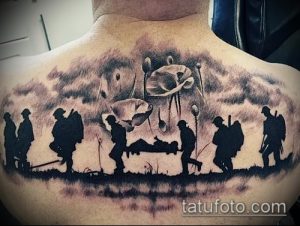 Фото тату на спине с изображением солдат на поле боя, среди маков. Реалистичный рисунок в черно-серых тонах, символизирующий память и жертву.