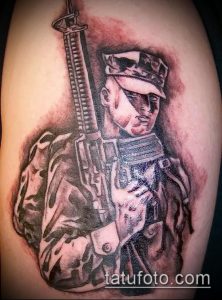 Фото тату на руке с изображением солдата в военной форме с винтовкой. Реалистичный черно-серый рисунок татуировки.