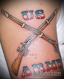 Фото тату на руке с перекрещенными винтовками и надписями 'US' и 'ARMY' в цветах американского флага. Детализированный рисунок татуировки.