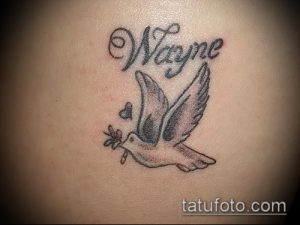 Фото тату: небольшой рисунок летящего голубя с оливковой ветвью и именем "Wayne", выполненный в черно-серых тонах. Персонализированная татуировка.