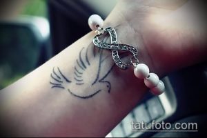 Фото тату на запястье: изящный голубь в полете и символ бесконечности, выполненные в минималистичном стиле черными чернилами.