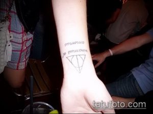 Черно-белое фото татуировки Даров Смерти и надписи на русском языке на руке. Простой, минималистичный рисунок татуировки.
