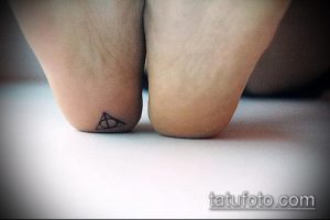 Фото тату: небольшая черно-белая татуировка Даров Смерти на лодыжке. Минималистичный дизайн, выполненный тонкими линиями.