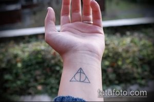 Фотография татуировки Даров Смерти, выполненной на запястье. Изображение представляет собой черный треугольник с кругом и линией внутри.