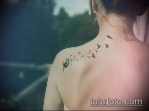 Фото татуировки на лопатке с изображением одуванчика, из которого вылетают птицы. Черно-белый рисунок, выполненный в технике лайнуорк.