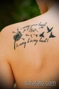 Фото татуировки одуванчика с летящими птицами и надписью 'i carry your heart (i carry it in my heart)' на плече. Черно-белый рисунок, выполненный в каллиграфическом стиле.