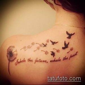 Фото татуировки одуванчика с летящими птицами и надписью 'Inhale the future, exhale the past' на спине. Черно-коричневый рисунок, выполненный в реалистичном стиле.