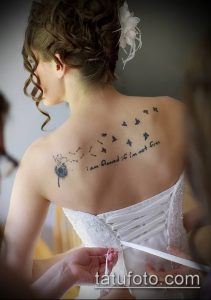 Фото татуировки одуванчика, летящих птиц и фразы 'I am flawed if I'm not free' на спине девушки.