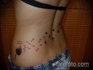 Фото тату одуванчика, из которого вылетают птицы, на женском боку. Черно-серый рисунок татуировки в минималистичном стиле.