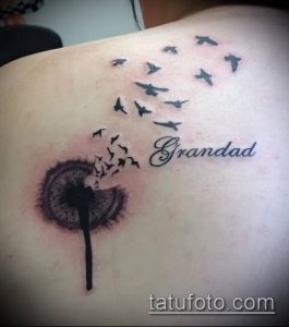 Фото тату одуванчика с улетающими птицами и надписью 'Grandad' на лопатке. Черно-белый рисунок, выполненный в реалистичном стиле, посвящен памяти близкого человека.