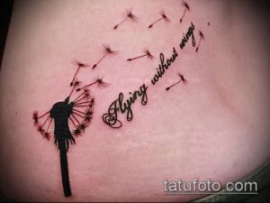 Фото тату одуванчика, из которого вылетают семена, с добавлением фразы "Flying without wings" на женском боку. Оригинальный и вдохновляющий рисунок татуировки.