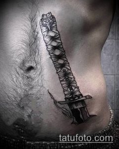 Фото тату на боку: катана, обвитая змеей, выполненная в технике blackwork. Четкие линии, минималистичный дизайн, контраст между кожей и черным цветом.