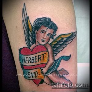 Фото тату: ангел с крыльями держит сердце с надписями "Herbert" и "Enid". Романтичная татуировка в стиле олд скул.