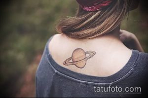 Фото тату Сатурна на спине. Небольшой рисунок планеты с кольцами, выполненный в коричневых и бежевых тонах. Элегантная и стильная татуировка.