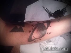 Фото татуировки Сатурна в процессе нанесения на руку. Черно-белый рисунок, планета с кольцами, тату-машинка.
