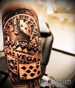 Фото тату казино на предплечье: рулетка, карты и надпись 'Welcome to Las Vegas'. Детализированный рисунок в черно-белой гамме.