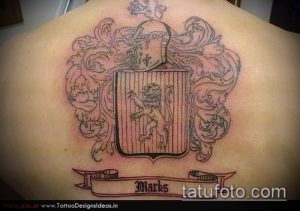 Фото татуировки на спине, изображающей геральдический щит с львом, украшенный декоративными элементами и надписью 'Marks'.
