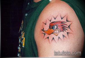 Фото тату с изображением головы мультяшного персонажа, окруженной взрывом, на плече человека. Яркие цвета и динамичная композиция.