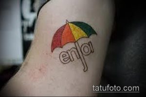 Фото татуировки зонта с надписью 'enjoy' на руке. Цветной рисунок татуировки в минималистичном стиле.