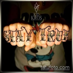 Фото татуировки с надписью 'Stay True' выполненной готическим шрифтом на костяшках пальцев. Черно-белый рисунок татуировки.