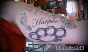 Фото татуировки кастета с отпечатками детских ног и надписью 'Harper'. Рисунок выполнен в черно-серых тонах.