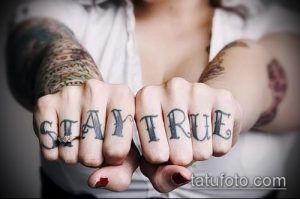 Фото тату: черная надпись 'STAY TRUE' на костяшках пальцев. Минималистичный дизайн, четкие линии, темная графика на светлой коже.
