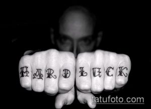 Фото тату надписи 'HARD LUCK' на костяшках пальцев. Черно-белый рисунок татуировки с готическим шрифтом.