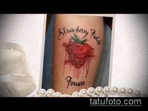 Фото тату клубники с каплями, стилизованными под кровь, и надписью 'Strawberry Fields Forever' на руке.