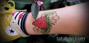 Фото тату клубники с цветами на запястье. Милый и женственный рисунок, выполненный в пастельных тонах.