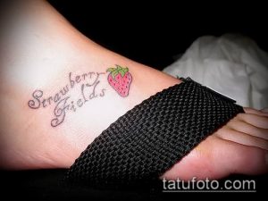Фото татуировки клубники с надписью 'Strawberry Fields' на лодыжке. Небольшой, стильный рисунок татуировки.